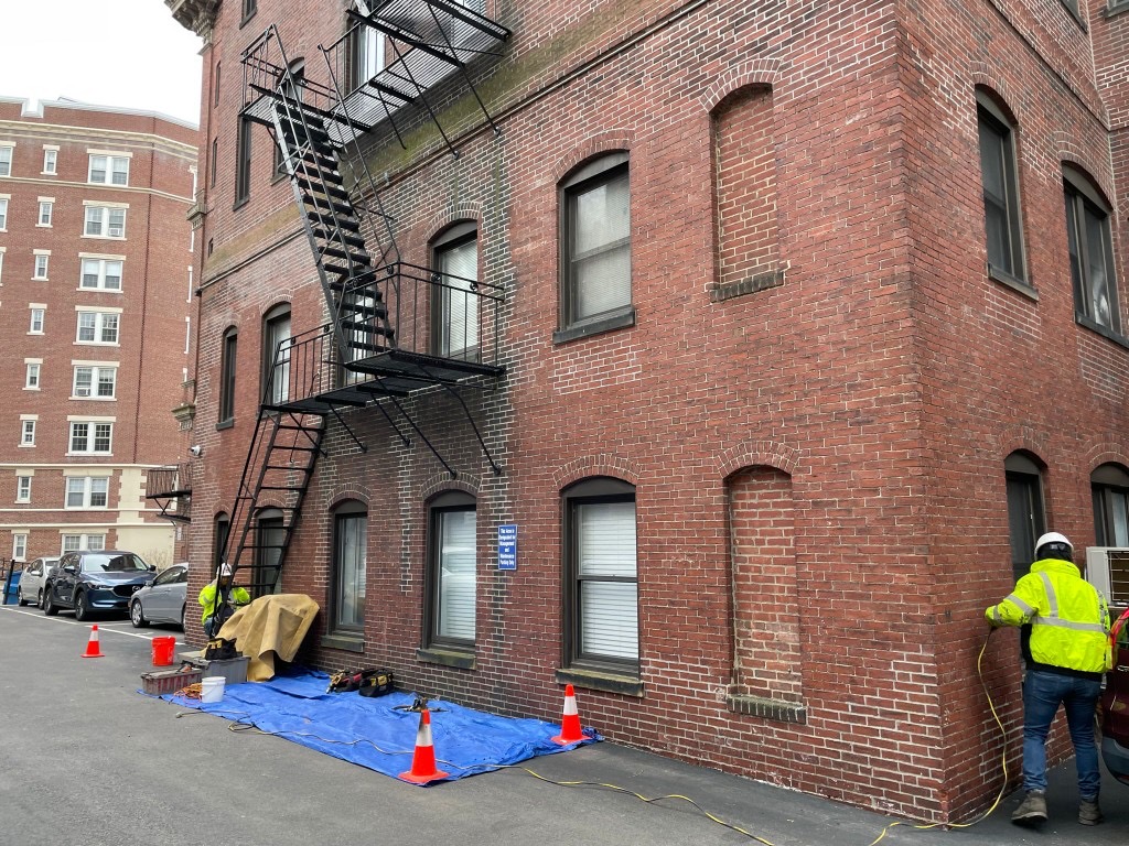 Commercial fire escape job site with safety cones, tarps, and technicians on a Boston brick building