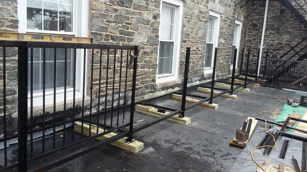 Fire escape railing fabrication and installation on a rooftop adjacent to a stone building