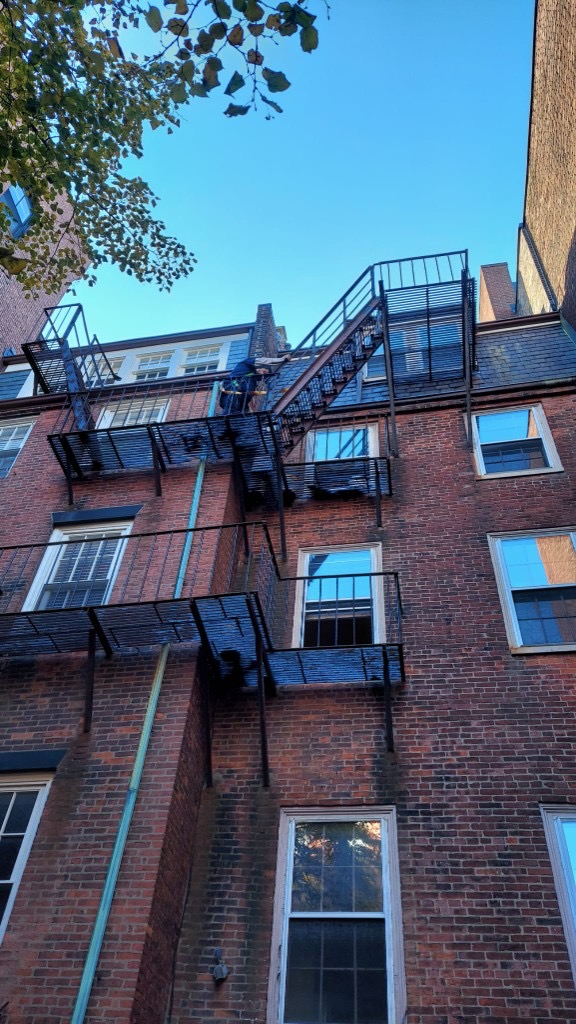 Worker in safety harness inspecting an elevated fire escape on a historic brick building